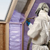Person in Full Protective Suit Spraying Foam Insulation Between Wall Studs
