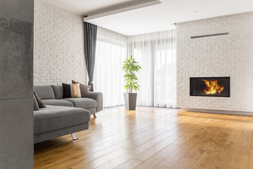 A living room with white brick walls, a fire place, and hardwoord flooring.