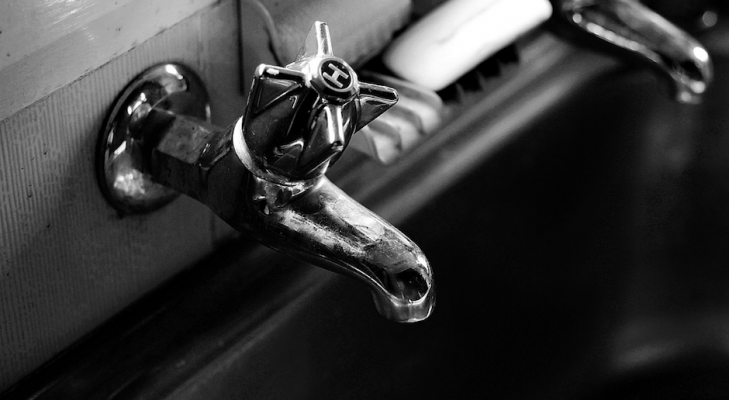 A black and white close up shot of a hot water faucet. 