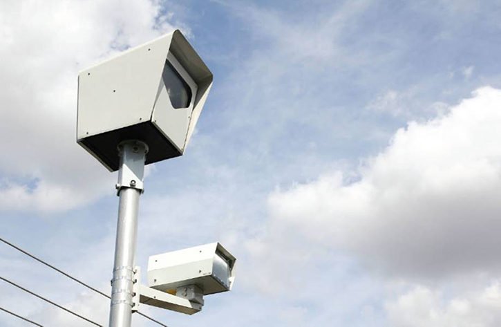 Red Light Camera Against Blue Sky with Clouds and Power Lines in Background