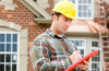 Contractor in Yellow Hard Hat Writing on Red Clipboard in Front of Brick House