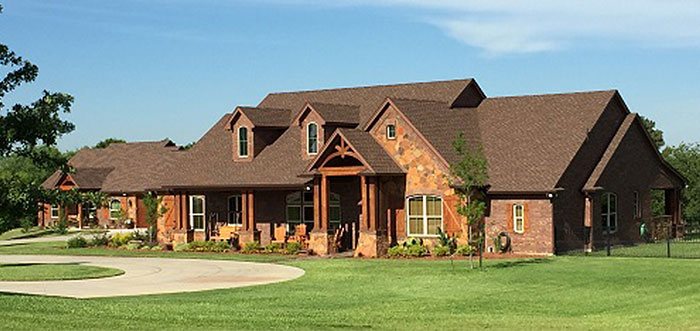 A large brown house with a driveway and a well-maintained lawn in front.