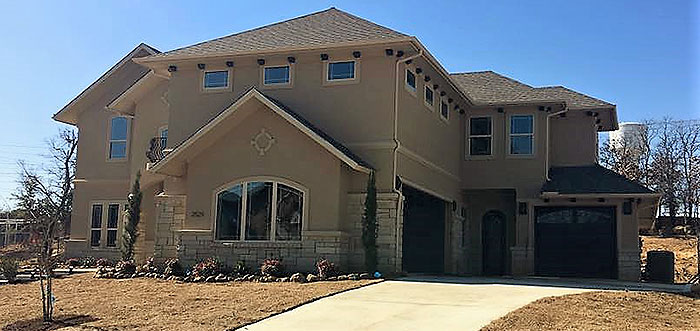 A large tan house featuring a driveway and an attached garage.