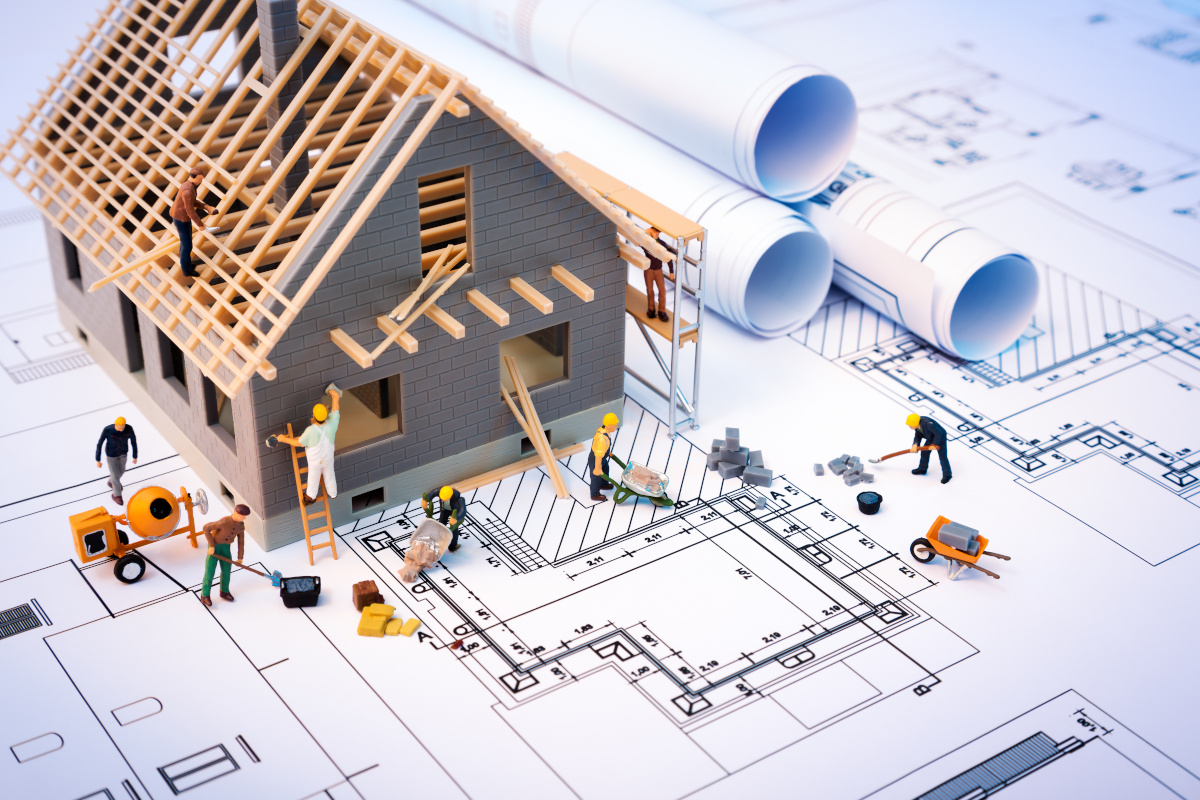 A blueprint with toy construction workers working on a toy house