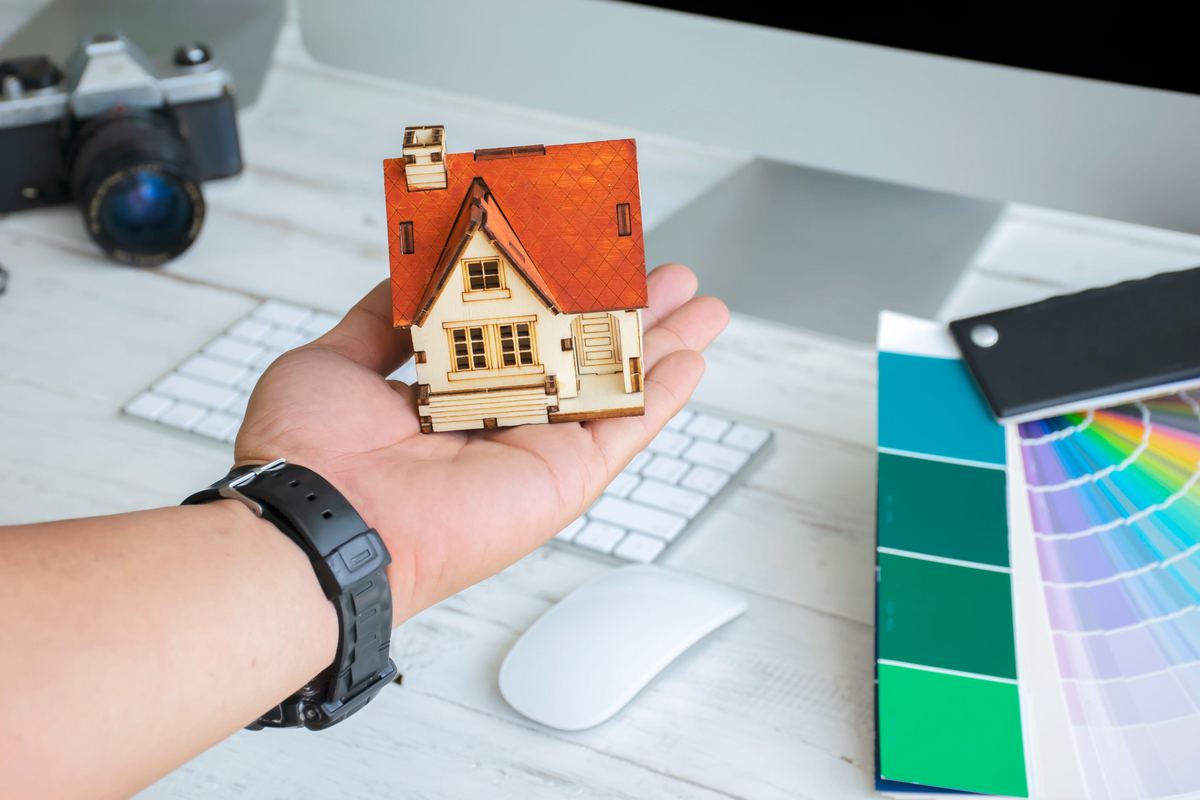 Hand holding a model house beside paint color swatches during a home design session.
