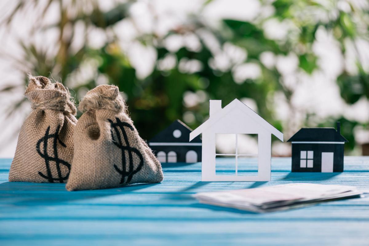 Two burlap money bags beside paper models of houses.