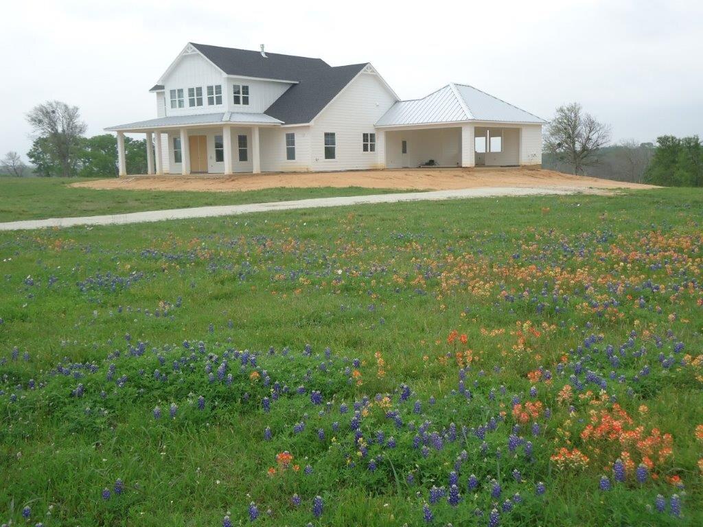 White farmhouse behind a field of bluebonnets and Indian paintbrush.