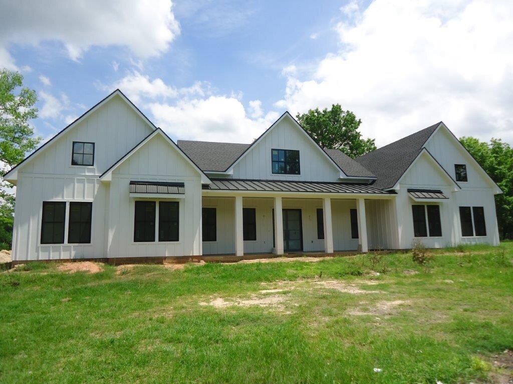 White farmhouse with a metal porch roof and a green lawn.