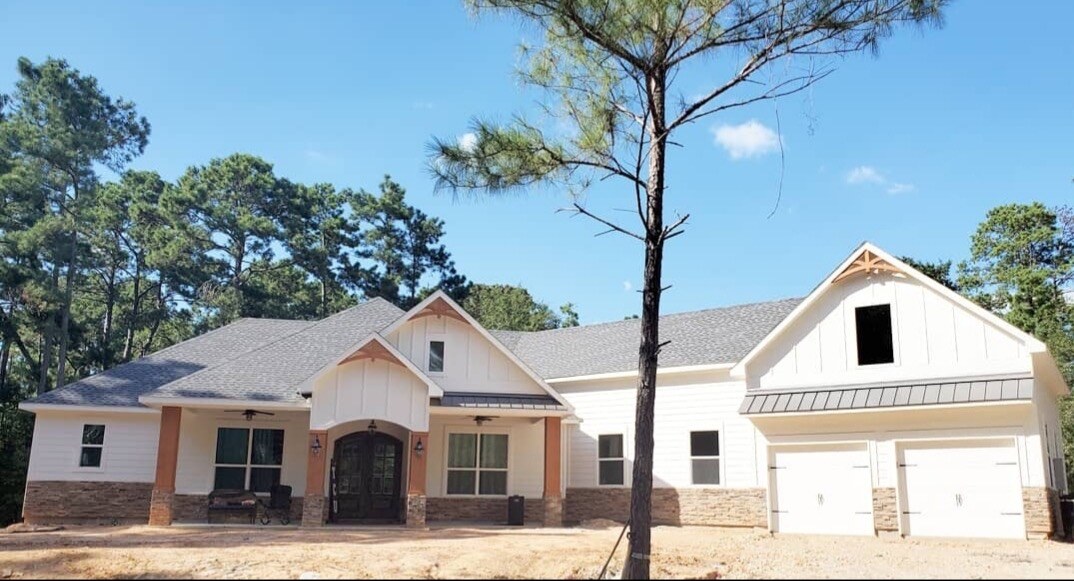 White farmhouse with stone wainscot and a double garage among pines.
