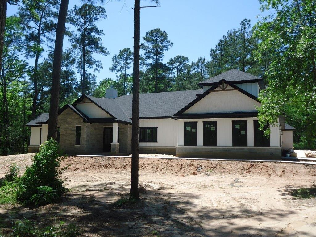 Stone and white ranch home under tall pines.