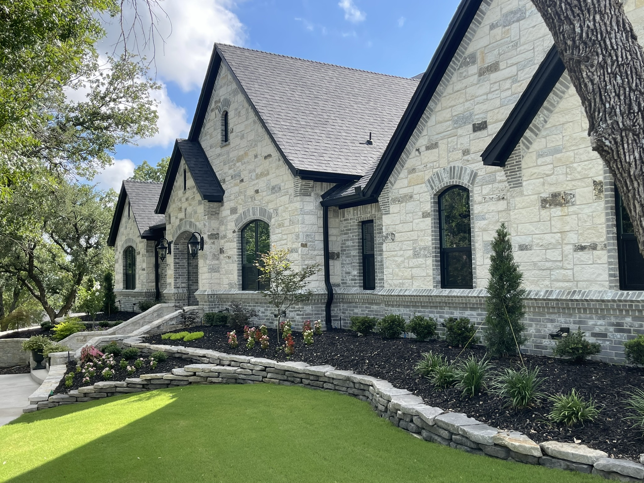 Front of a stone house with green lawn and matching stone retaining wall